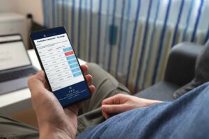 En person sidder med en smartphone og ser på en skærm, der viser en oversigt over inkassoprocesser med fakturaoplysninger. Billedet illustrerer håndtering af inddrivelsesprocessen via inkassoadvokat.dk.